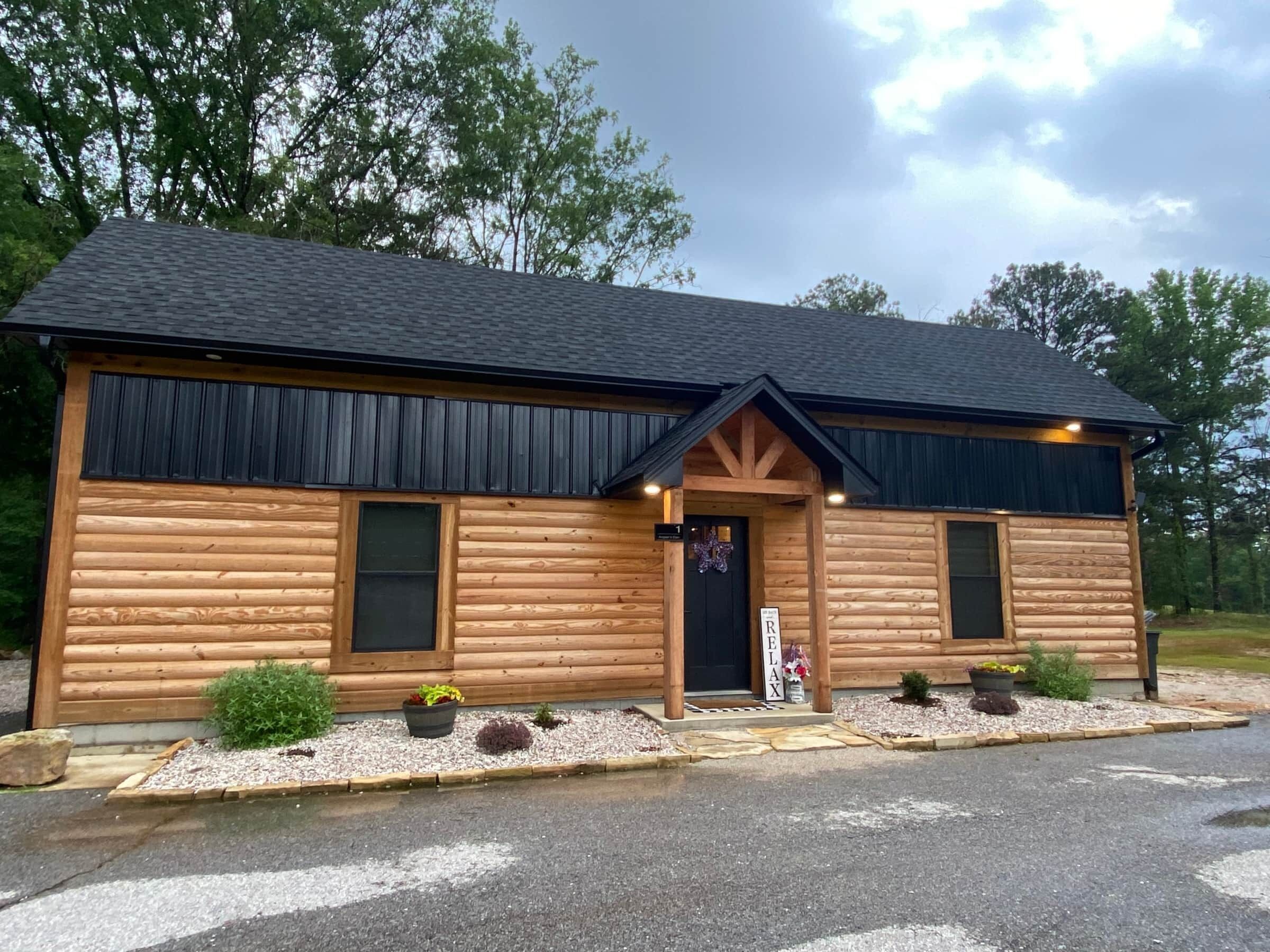 A log cabin with a black roof, two windows, and a door.
