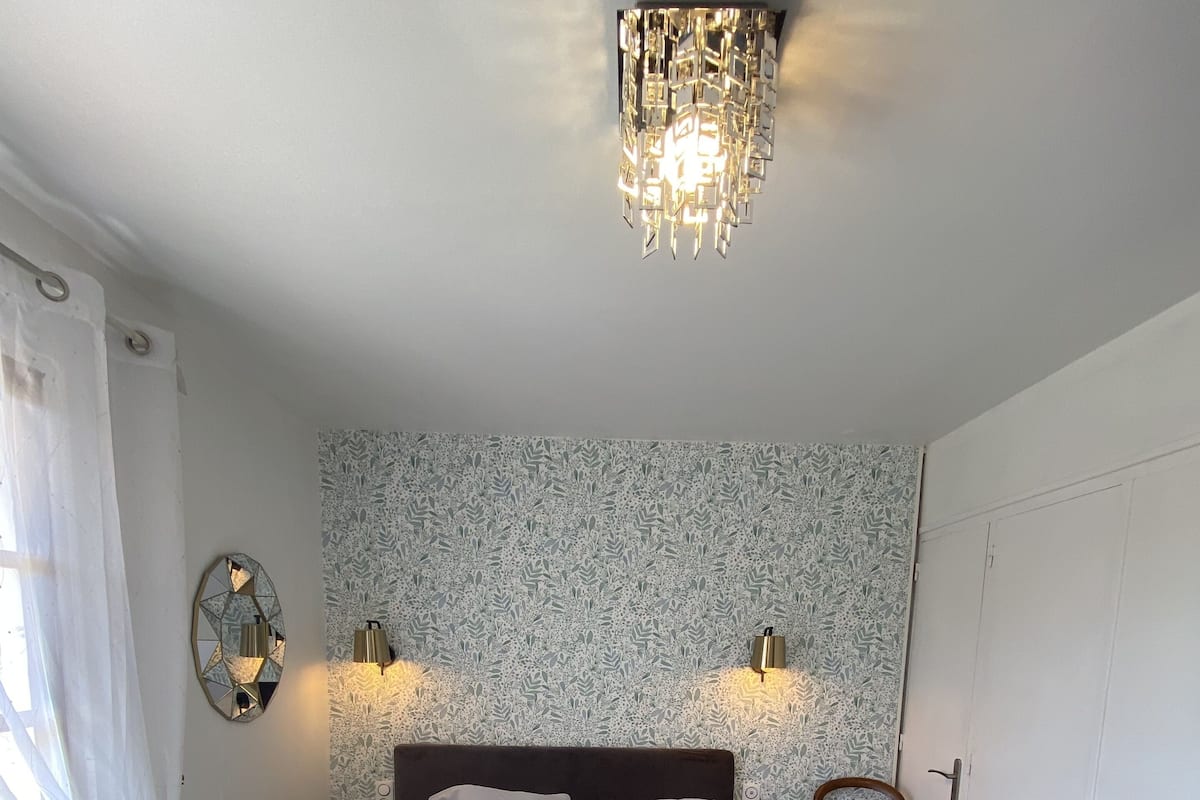 Une chambre avec un grand lit, deux appliques murales, un miroir décoratif, un radiateur et une chaise en bois.