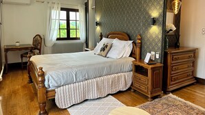 Een slaapkamer met een groot bed, een houten dressoir, een bureau en een raam met gordijnen.
