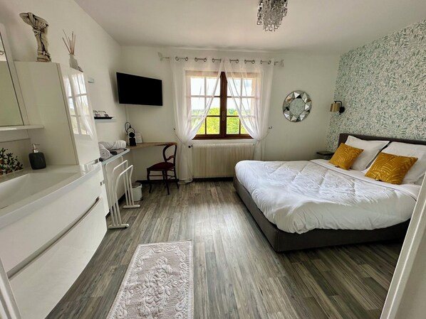 Une chambre à coucher avec un lit, un bureau, une chaise, un téléviseur et une fenêtre avec des rideaux.