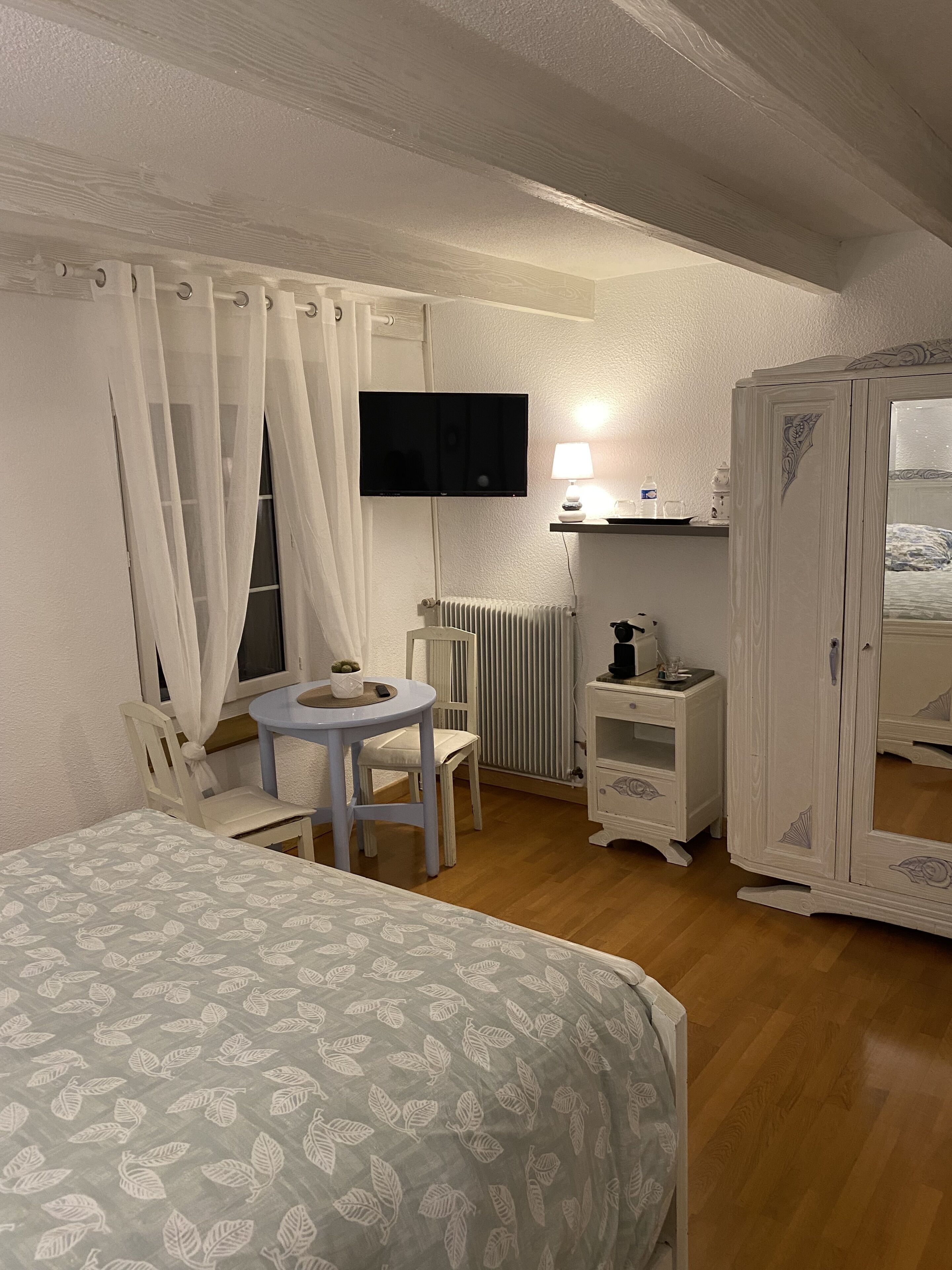 A bedroom with a bed, a desk, a chair, a TV, a wardrobe, and a radiator.