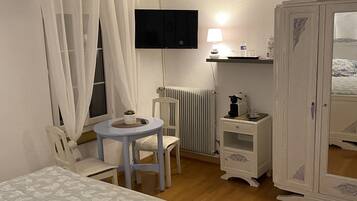 A bedroom with a bed, a desk, a chair, a TV, a wardrobe, and a radiator.