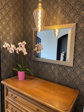 Une coiffeuse avec un miroir, une plante orchidée rose et un luminaire décoratif.