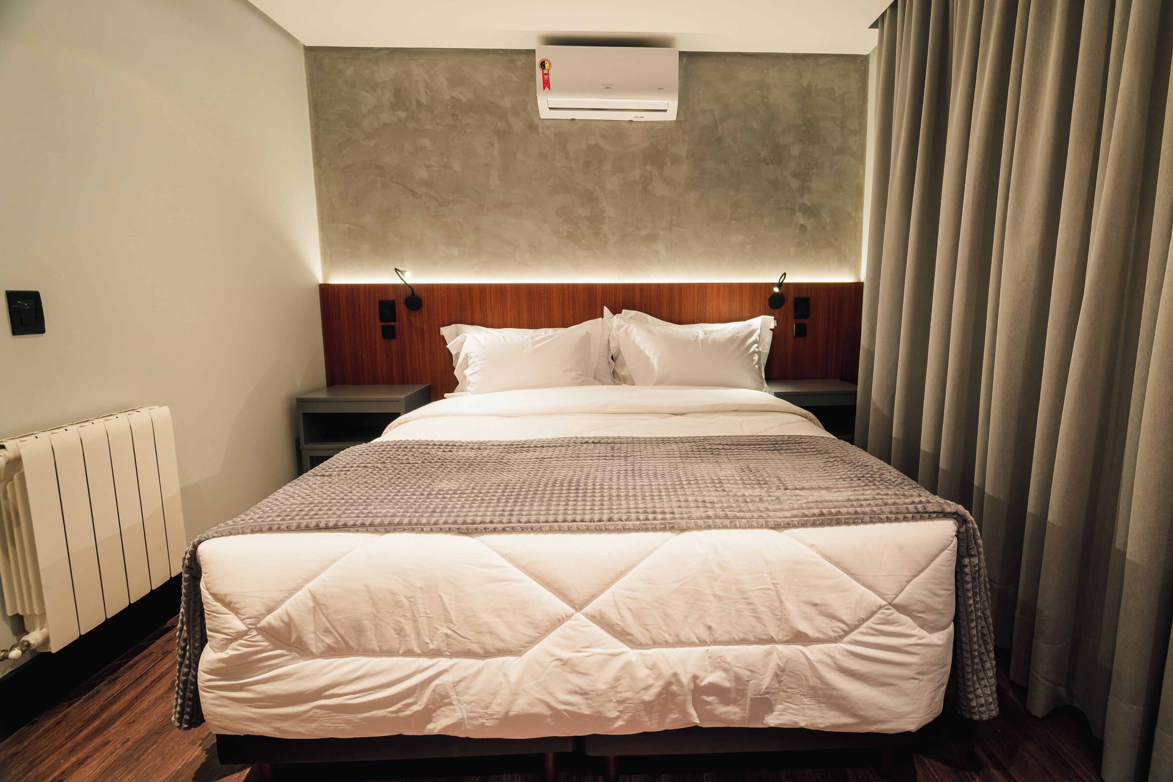 Habitación de hotel con una cama grande, cabecera, aire acondicionado de pared y ventana con cortinas.