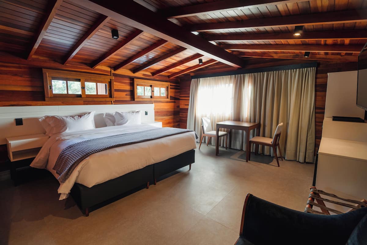 Un dormitorio tipo cabaña de madera con una cama grande, una mesita pequeña con sillas y un televisor.