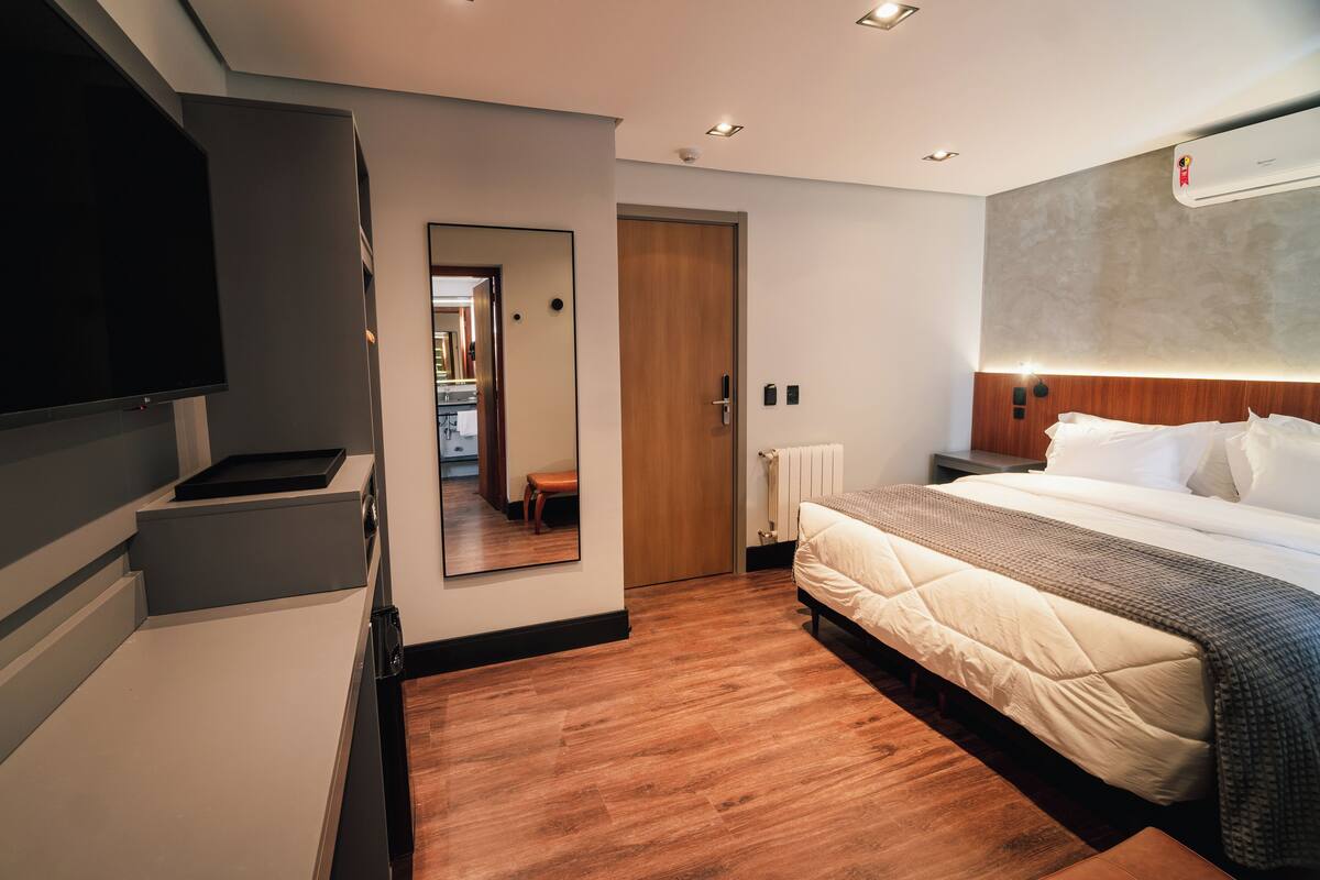 Una habitación de hotel moderna con una cama grande, un televisor de pantalla plana, piso de madera y un espejo.