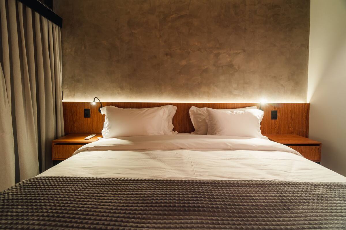 Una habitación de hotel con una cama grande, cabecera de madera, dos mesitas de noche y una mesita auxiliar.