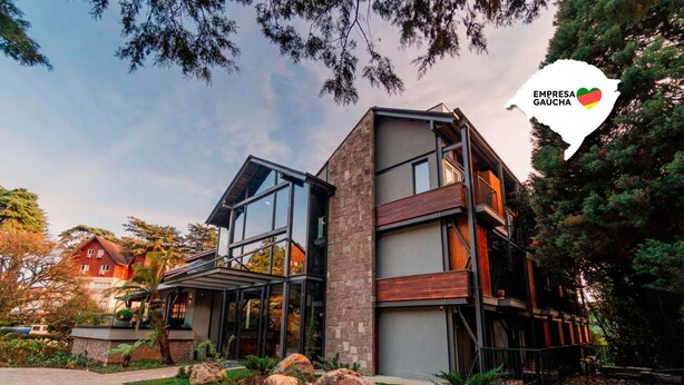 A modern multi-story building with large glass windows, a stone facade, and a landscaped garden with rocks and shrubs. - 249 DESIGN HOTEL (Gramado)