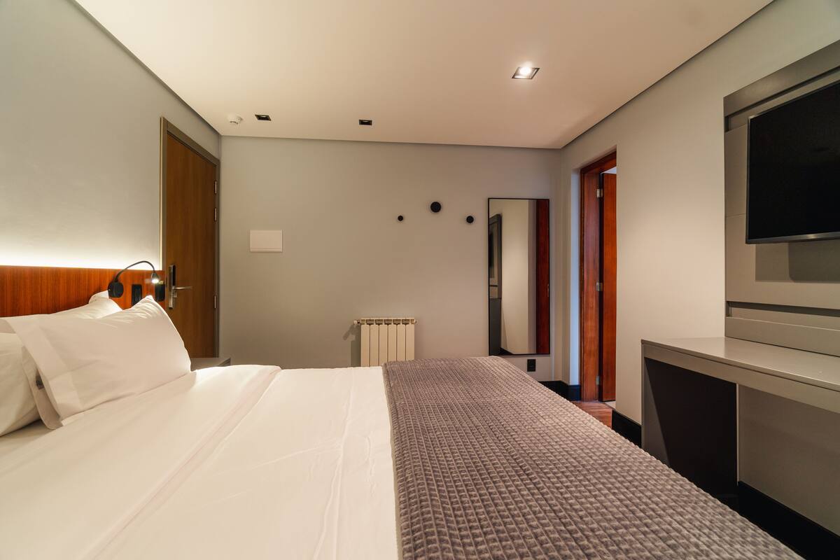 Una habitación de hotel con una cama, una mesita de noche, un televisor y un espejo.