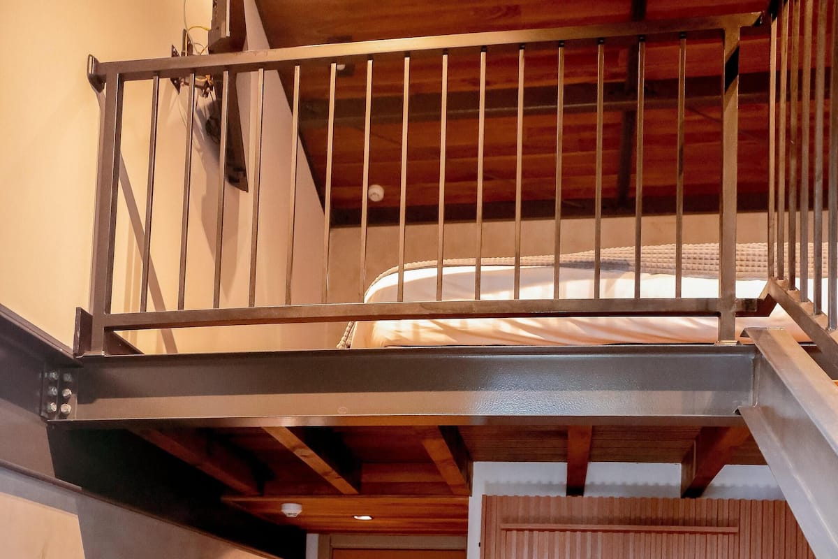 Un espacio tipo loft con piso de madera, una silla de estructura metálica, una pequeña mesa de madera y una escalera que conduce a un nivel superior.