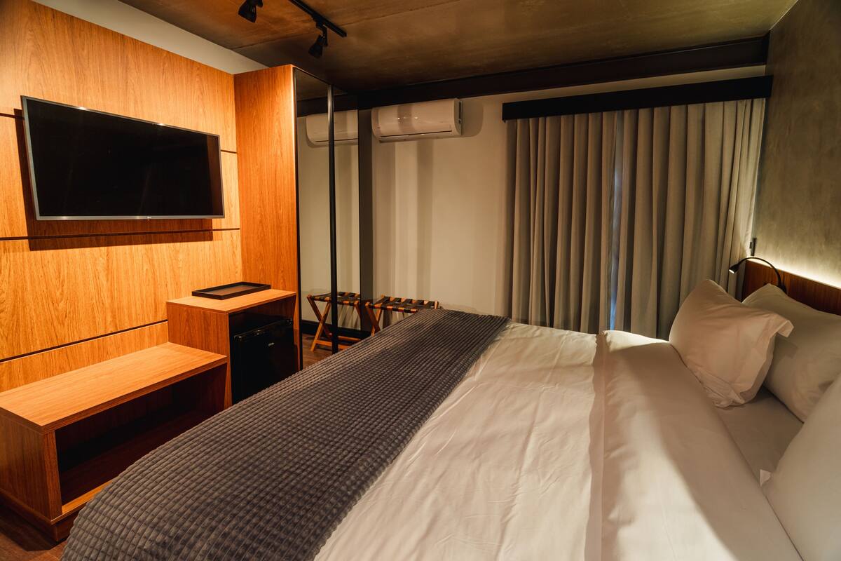 Una habitación de hotel con una cama grande, un televisor instalado en la pared, un escritorio y una silla.