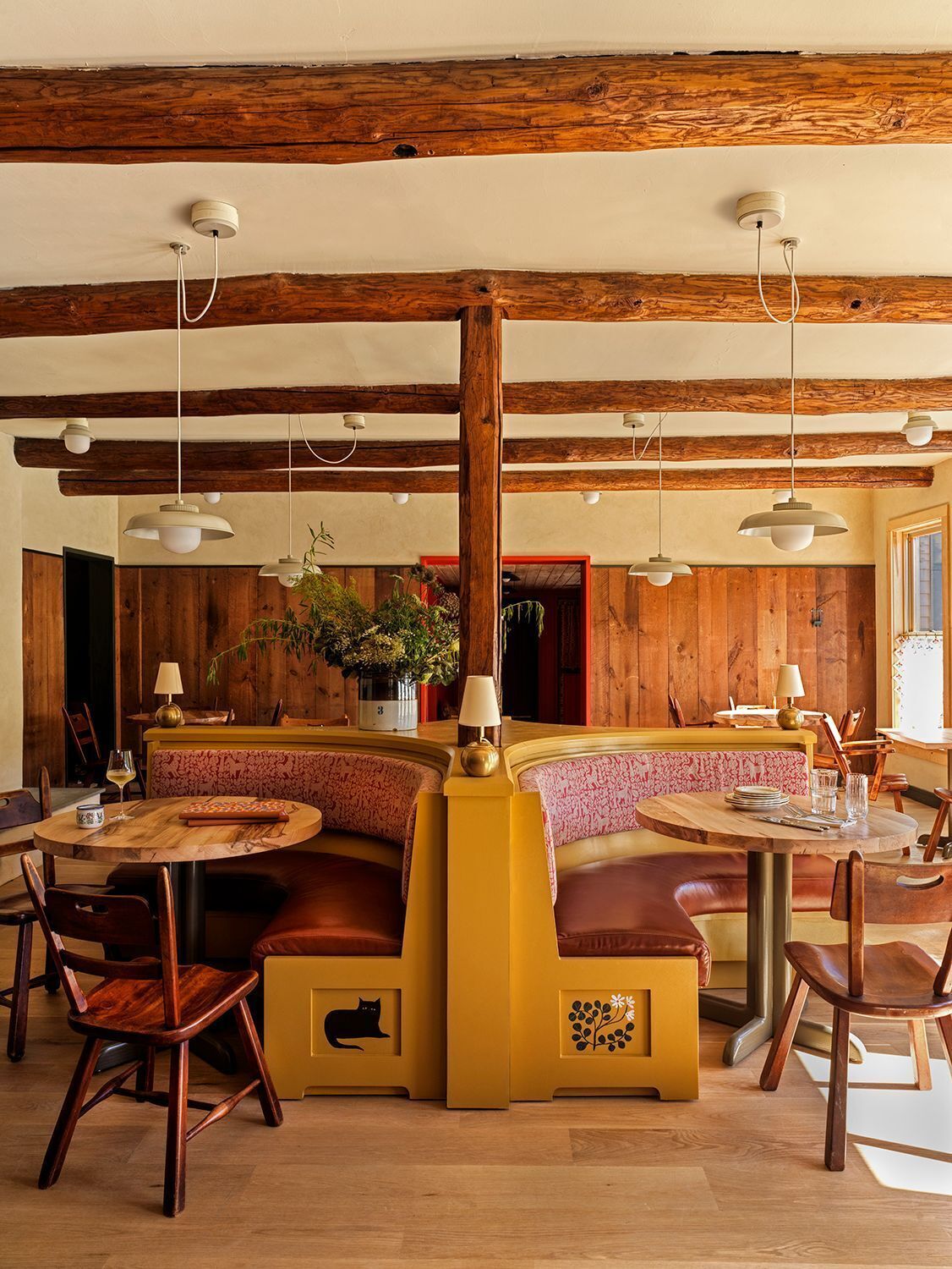 A restaurant with wooden beams, round tables, and booths.