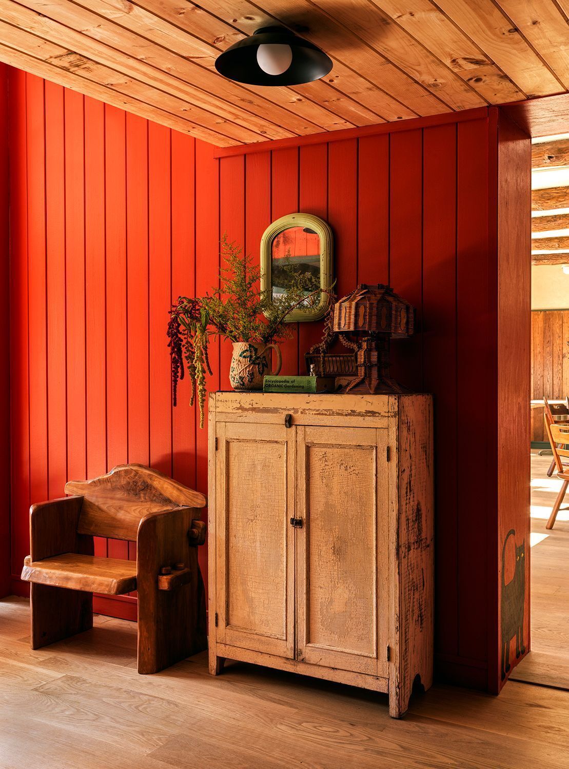 A room with a wooden cabinet, a chair, and a mirror on a red wall.