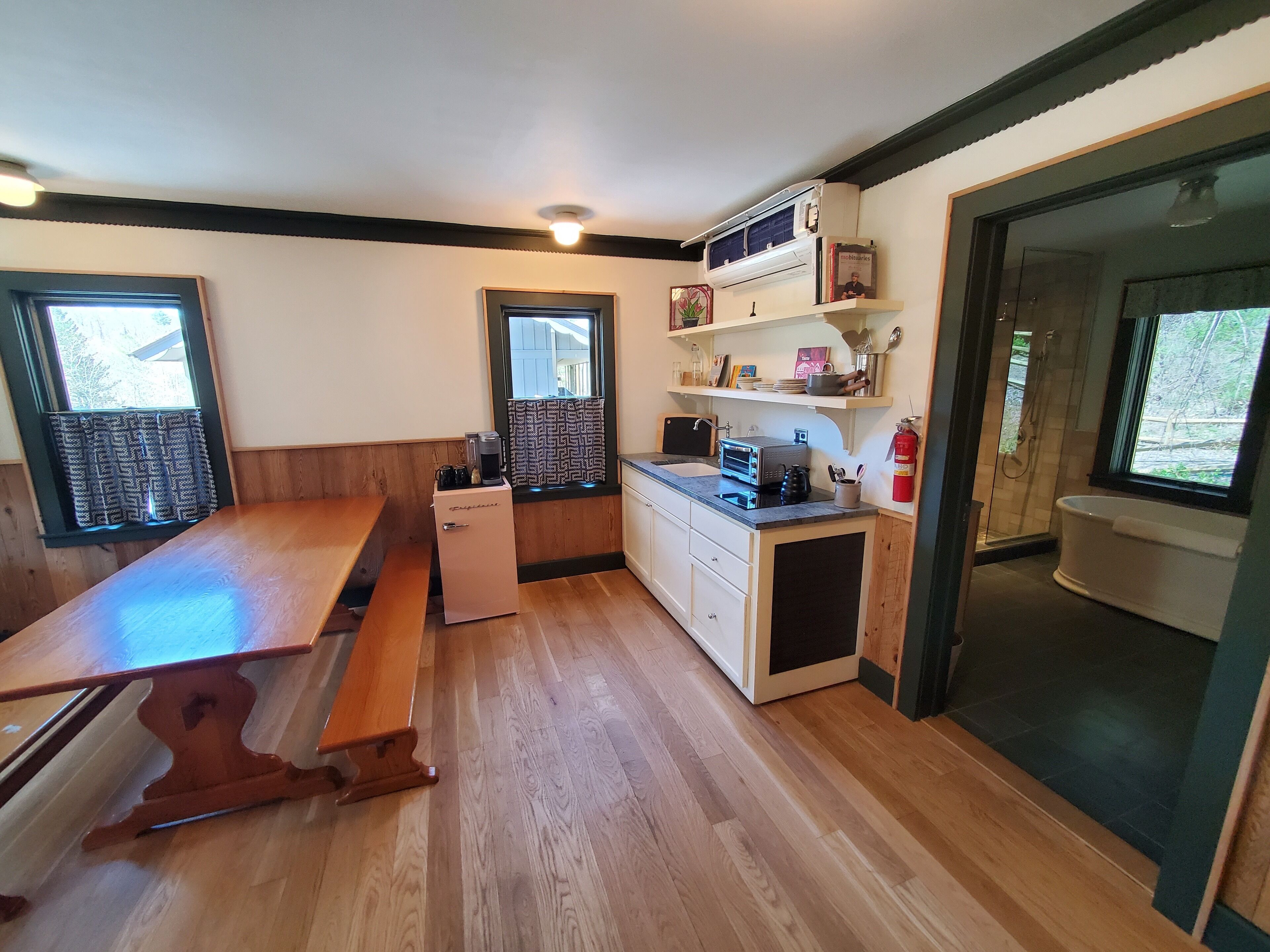 Uma cozinha compacta com piso de madeira, um banco embutido, geladeira, torradeira e janela com cortinas estampadas.