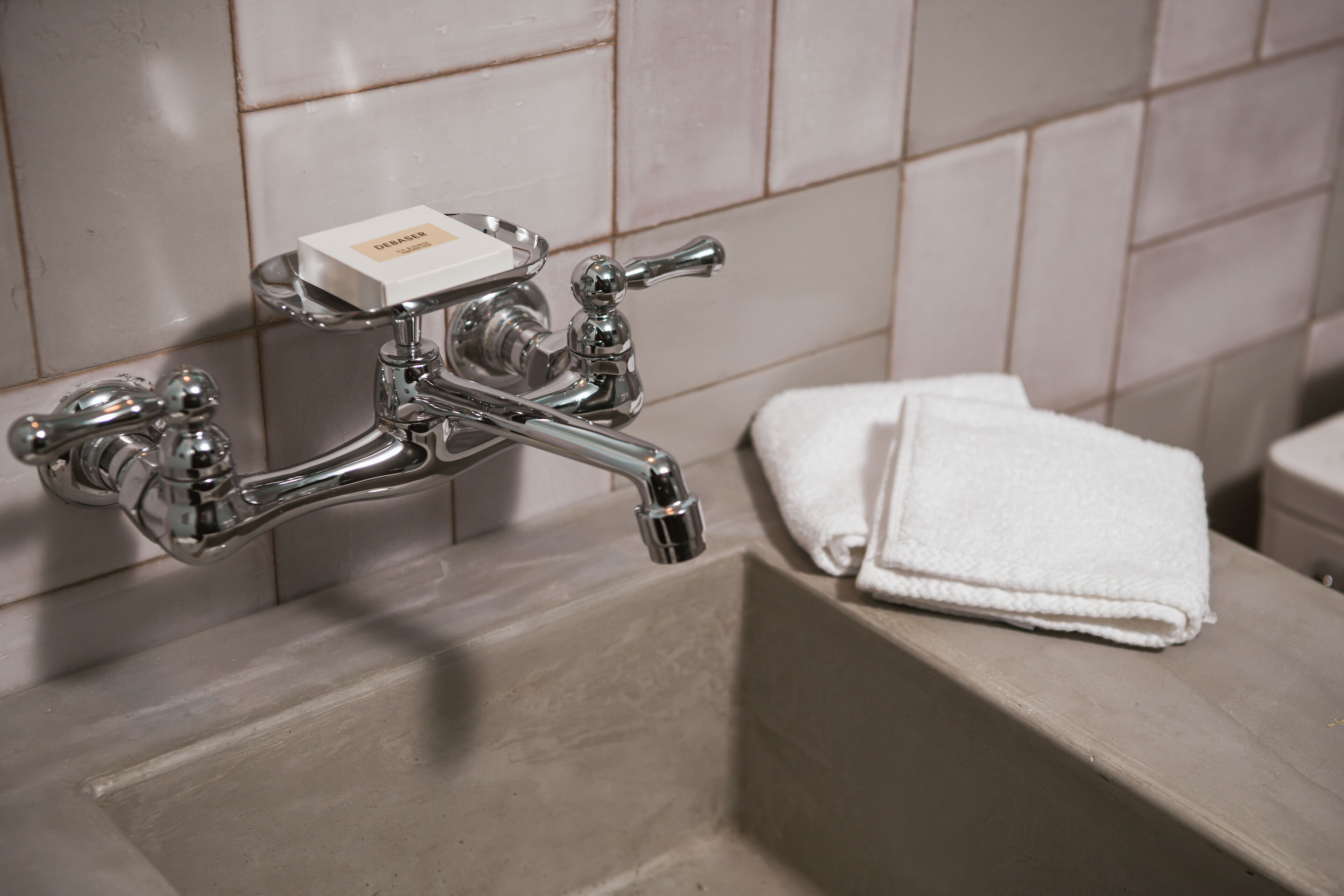 Un baño con un grifo cromado, un jabonera y una toalla blanca sobre una encimera.