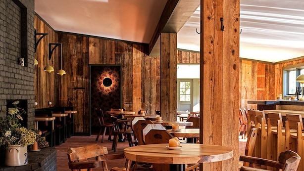 Ein rustikales Interieur mit Holztischen und -stühlen, Backsteinwänden und einer großen Holzbalkenkonstruktion.