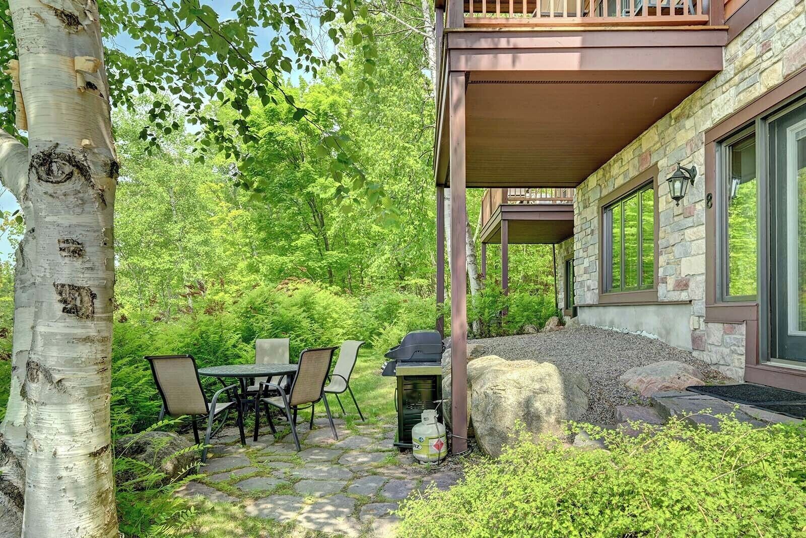 Un patio de piedra con mobiliario exterior, una parrilla y un muro de piedra.