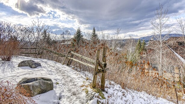Un paysage enneigé avec une clôture en bois, des rochers et une végétation clairsemée.