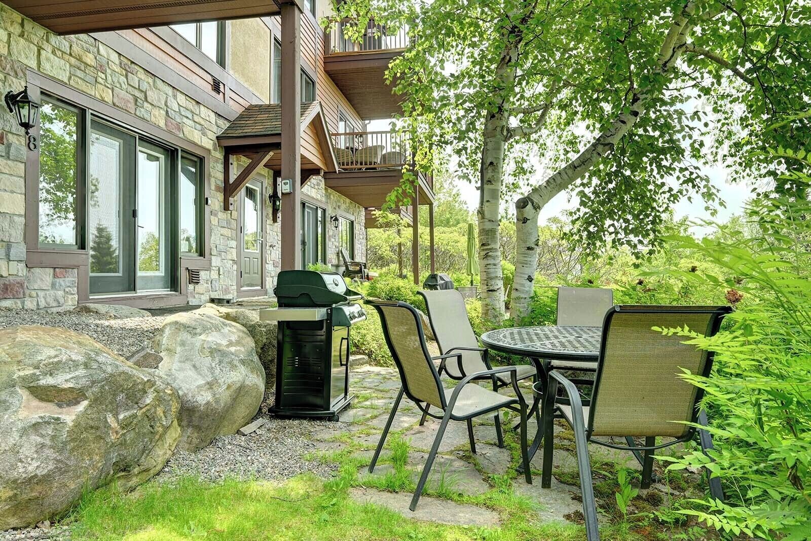 A patio with a grill, outdoor seating, and a stone wall.