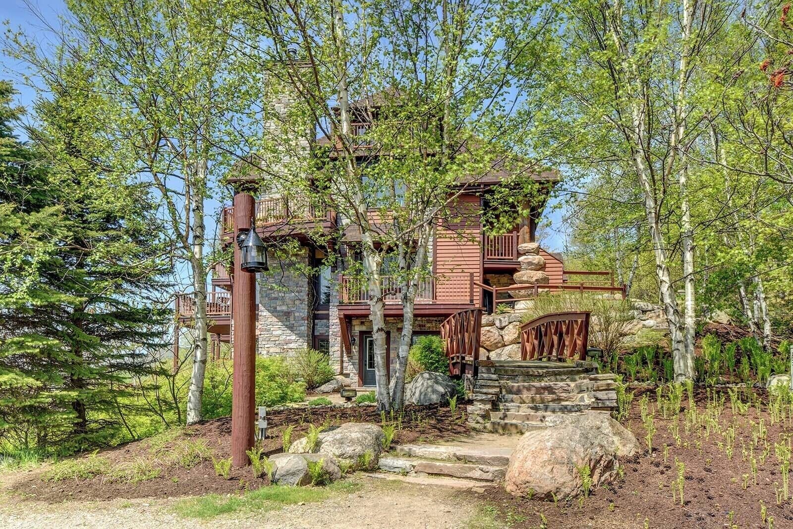 Un chalet rustique avec des fondations en pierre, des balcons en bois et un escalier en bois menant à l’entrée.