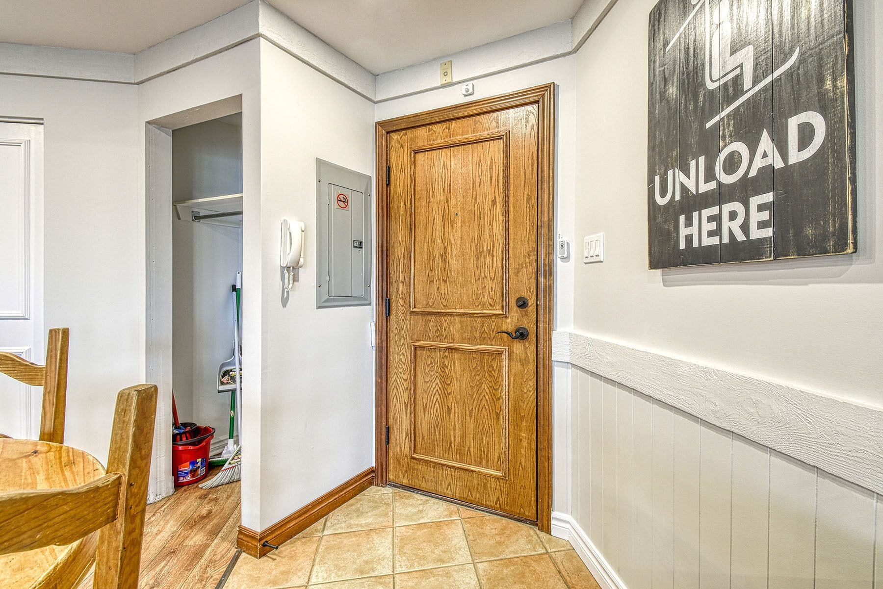A hallway with a wooden door, a 'UNLOAD HERE' sign, a telephone, and a trash bin.