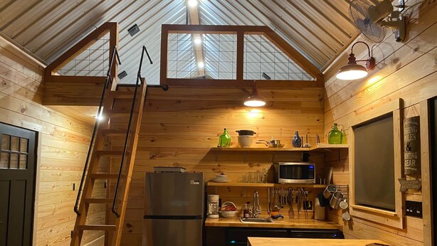 Eine gemütliche, blockhausartige Küche mit Holzwänden, einer Dachkuppel, einem Kühlschrank, einer Mikrowelle und einem Essbereich mit Hockstühlen.