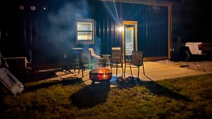 Ein Sitzbereich im Freien mit Feuerstelle, Stühlen und Tisch.