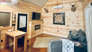 Ein gemütliches Blockhauss Innenleben mit Holzbalkendecke, Esstisch, Sofa und aufgehängtem Hirschkopf.