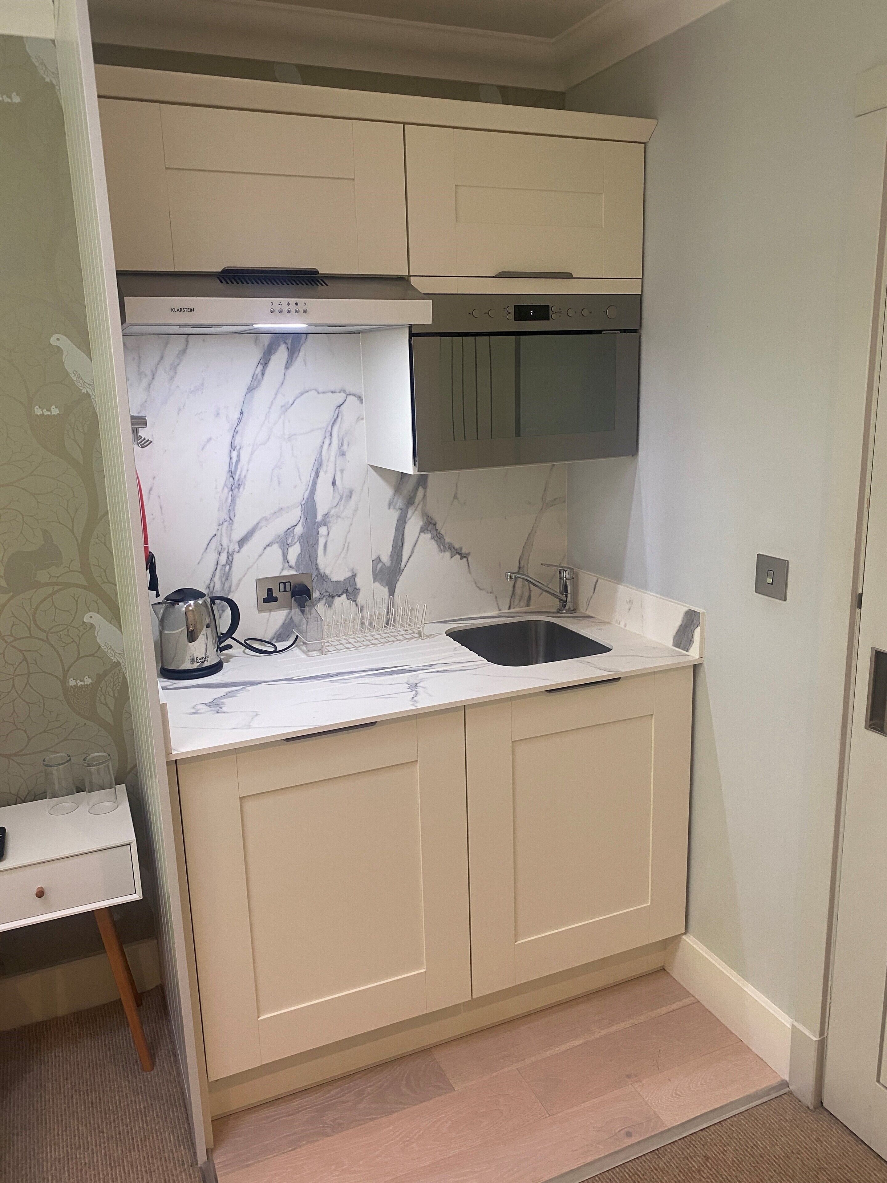 A compact kitchen with a marble backsplash, a built-in oven, and a stainless steel sink.