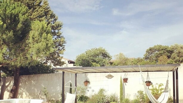 Un espace aménagé au bord de la piscine, comprenant un coin salon couvert, un hamac et des plantes en pot.