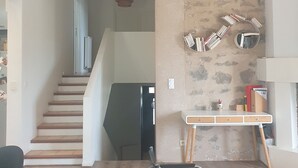 Un salon moderne avec un escalier, une table en bois, une chaise noire et une bibliothèque.