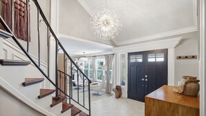 A staircase with wooden steps and black railings, a chandelier, a dark door, and a wooden side table with a vase. - 6BR SoCal Oasis with Pool Spa Sauna (Mission Viejo)
