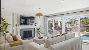 A living room with a fireplace, a sofa, a coffee table, and a view of the outdoor patio. - 6BR SoCal Oasis with Pool Spa Sauna (Mission Viejo)