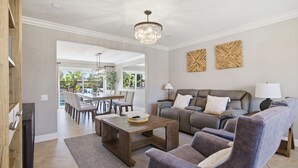 A modern living room with a sofa, armchairs, a coffee table, and a chandelier. There is a dining area with a table and chairs visible in the background. - 6BR SoCal Oasis with Pool Spa Sauna (Mission Viejo)