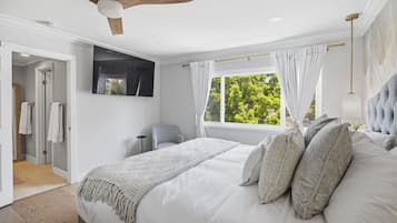 Une chambre à coucher avec un lit, un ventilateur de plafond, une fenêtre avec des rideaux et une vue sur les arbres.