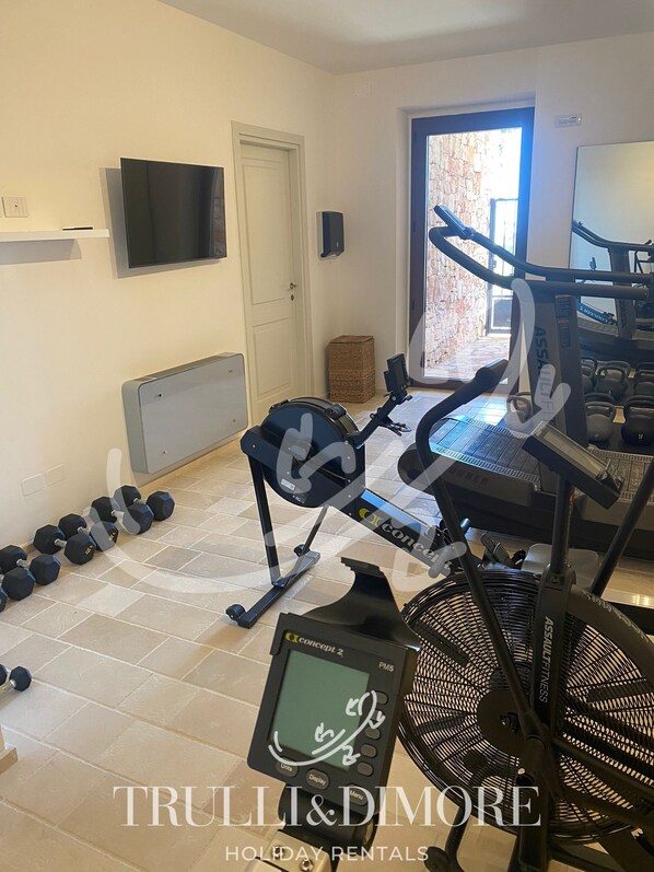 Un gimnasio en casa con equipo de ejercicio, un televisor y una puerta que da a un muro de piedra.