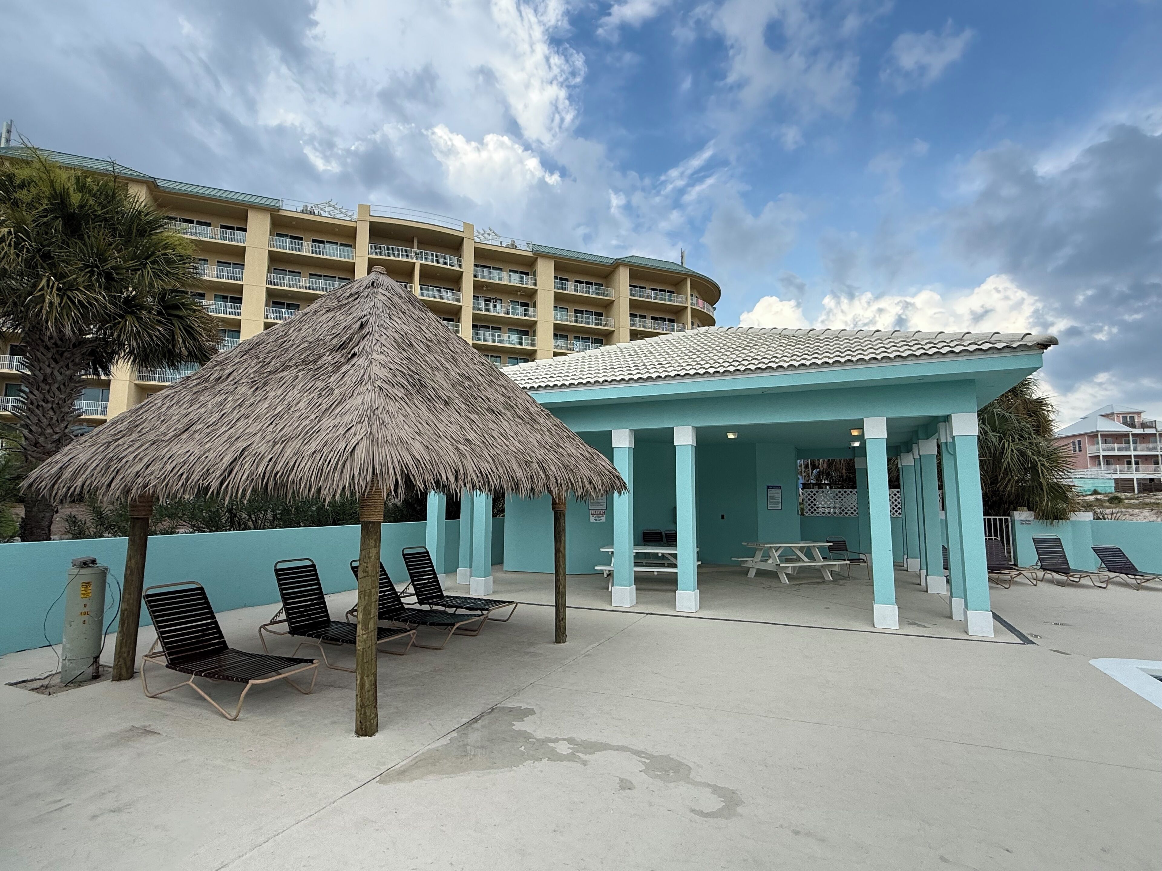 A beachside building with a thatched roof and lounge chairs.