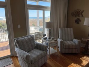 Une chambre avec vue sur l’océan, un balcon, deux fauteuils à rayures, une petite table avec une lampe et un décor mural représentant des poissons.