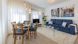 Una sala de estar moderna con una mesa de centro de vidrio, un sofá azul y un comedor con sillas de madera.