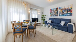 Ein modernes Wohnzimmer mit einem Glastisch, einem blauen Sofa und einem Essbereich mit Holzsesseln.