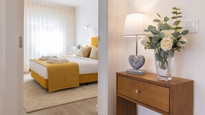 A hotel room with a bed, bedside table, lamp, and a vase with flowers.