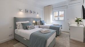 A modern bedroom with two beds, a desk, and a TV.