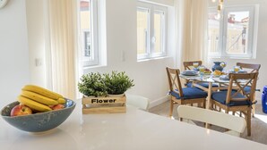 Comedor con una mesa dispuesta para dos, un frutero y una planta en maceta con la etiqueta 'Flower'.