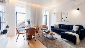 Una sala de estar moderna con un sofá azul oscuro, una mesa de centro y una zona de comedor con sillas y una mesa preparada para dos comensales.