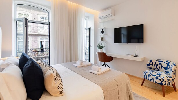Una habitación de hotel moderna con cama, televisión, sillón y balcón.