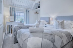 Two single beds with matching headboards and a functional workspace with a dresser, mirror, and lamp.