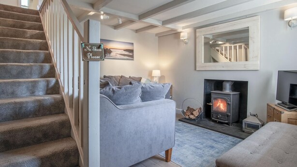 A living room with a grey sofa, a fireplace, a television, and a staircase. - Dollars Cottage - 4 Bedroom Cottage - Llangennith (Swansea)