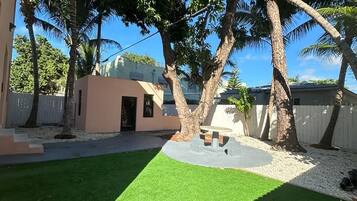 A backyard with artificial grass, a small patio area, and palm trees.