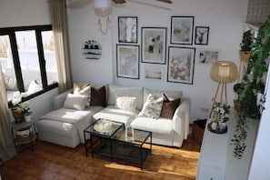 Un salon moderne avec un canapé blanc, une table basse en verre et des œuvres d’art accrochées aux murs.