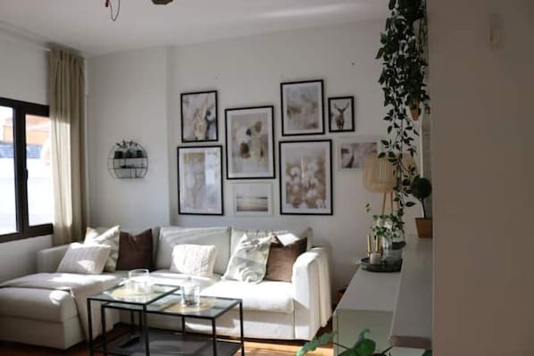 Un salon avec un canapé blanc, une table basse en verre et des œuvres d’art encadrées accrochées au mur.
